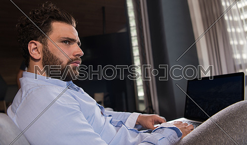 technology, home and lifestyle concept  of man working from home using laptop computer and sitting on sofa