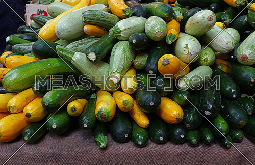 Close up fresh new green and yellow zucchini on retail display of farmers market, high angle view