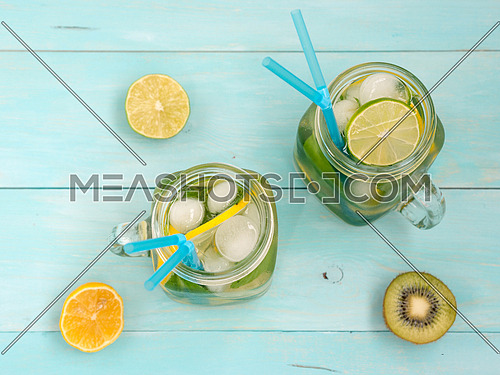 Cold homemade lemonade with fresh lemon, lime, kiwi and mint in mason jar. Summer drink on soft blue wooden background. Flat lay or top view
