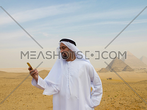 young man as tourist  wearing  arabian traditional clothes in egypt with giza pyramids in background  using smartphone