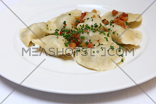 Plate of pierogi or varenyky stuffed filled dumplings with bacon crisps and green chive onion, traditional East Europe cuisine meal popular in Poland, Ukraine, Slovakia, Russia, close up, high angle view