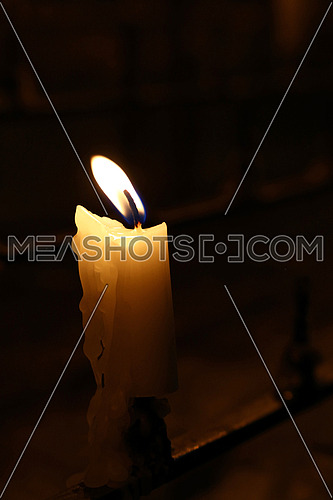 One white candle with melting wax burning in dark church, close up, high angle view
