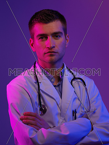 Portrait of hero in white coat.  Cheerful smiling young doctor with stethoscope in medical hospital standing against blue and pink background. Coronavirus covid-19 danger alert