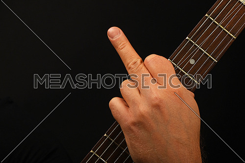 Man hand holding guitar neck with finger fuck off insult ignore gesture over black background