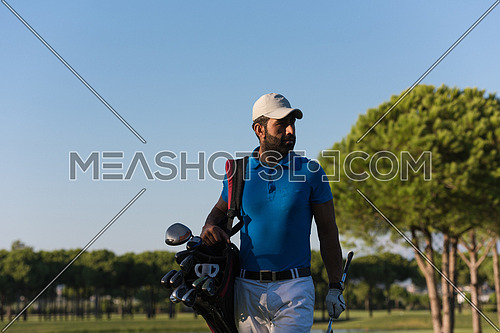 handsome middle eastern golfer carrying  bag  and walking to next hole at golf  course