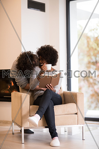 Young beautiful multiethnic couple hugging in front of fireplace at home when reading a book at autumn day