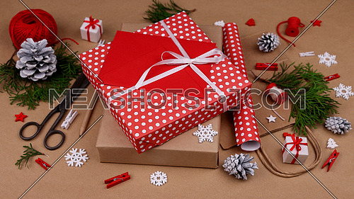 Close up packing and wrapping Christmas gift boxes with red paper and adding envelope, high angle view