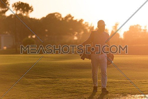 handsome middle eastern golfer  carrying  bag  and walking  to next hole at golf  course on beautiful sunset in background