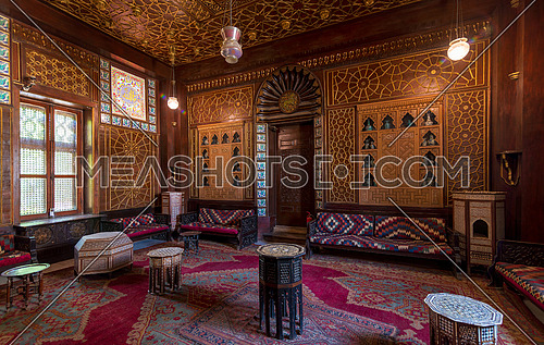 Manial Palace of Prince Mohammed Ali. Guests Hall with wooden ornate ceiling, wooden ornate door, lanterns, colorful ornate couches, tea tables and ornate carpet, Cairo, Egypt