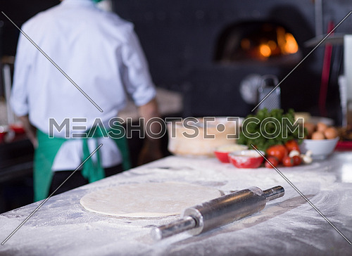 chef preparing dough for pizza rolling with hands on sprinkled with flour table