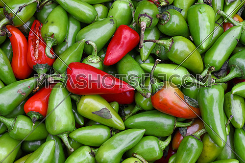Close up heap of many fresh green and red hot jalapeno chili peppers on retail display at farmers market, elevated top view, directly above