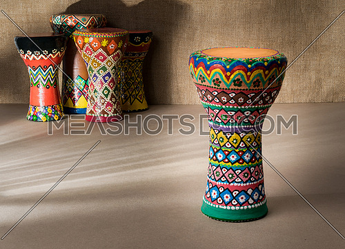 Front view of decorated colorful pottery goblet drum on background of goblet drums, wooden table with vanishing shadow lines, and sackcloth wall