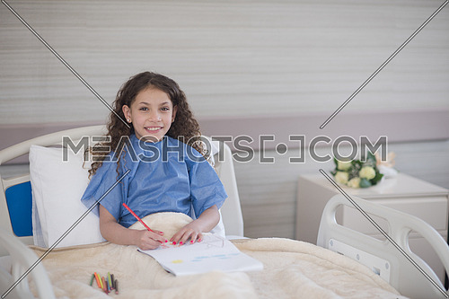 little middle eastern girl painting home and family at hospital bed in a large modern hospital