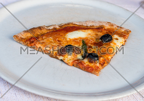In the picture a slice of pizza with tomato, mozzarella cheese and olives served on a white dish at the restaurant.