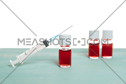 medical vaccine phials with red liquid and syringe over green table and white background. Vaccination and immunization conceptual.