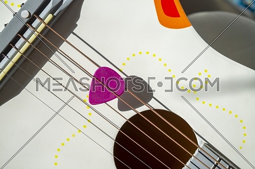 Colorful pink plectrum in guitar strings in a close up top angle view and hard shadows in a music and entertainment concept
