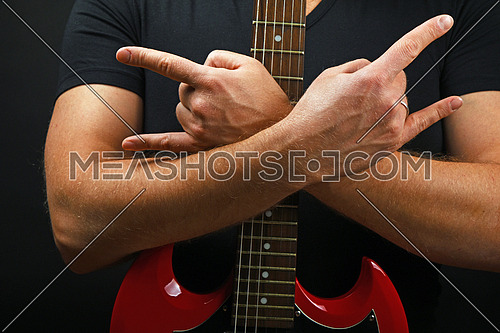 Man hands holding embracing red sg guitar neck with devil horns rock metal sign over black background