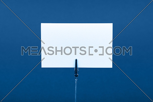 Blank white cardboard sign with copy space on classic metal note holder over dark blue paper background, front side view