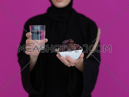 Modern Muslim Woman in Abaya Holding a Date Fruit and glass of water in from of her. Concept celebration of iftar in ramadan and end of feasting