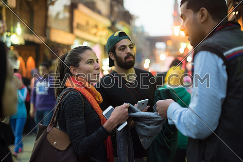 Young middle eastern tourists enjoy the city and talk to traders in the traditional street market