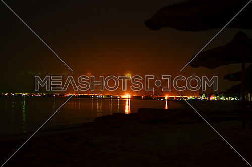 Long exposure view of the beach with lined hay sunshades and the city appears at the far end
