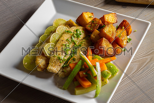 A dish of Fish fillet and potato cubes served with vegetables and lemon slices