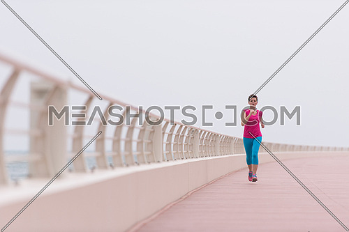 very active young beautiful woman busy running on the promenade along the ocean side to keep up her fitness levels as much as possible