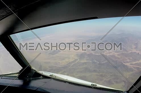 Close shot from inside plane cockpit showing sky horizon from the window and desert at day