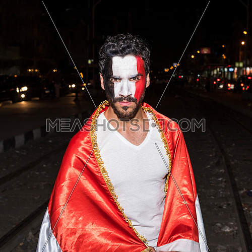 young man cover himself with big egyptian flag and has a paint for egyptian flag on his face in korba area at night
