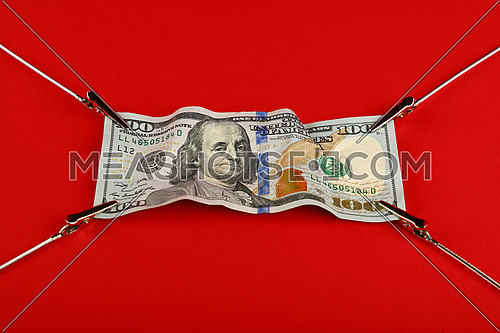 Close up one hundred US dollar paper currency banknote pulled and stretched over red background with copy space, high angle view
