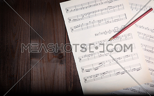 In the picture aged pages of sheet music, pencil  and wooden background, above view.
