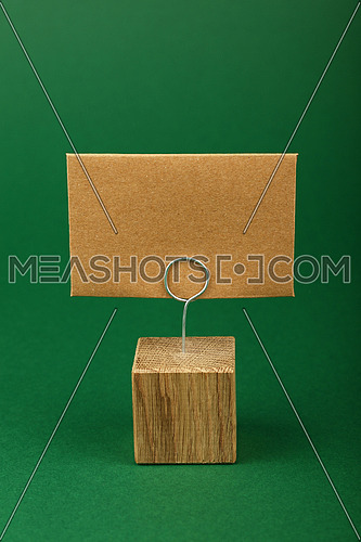 Blank brown kraft cardboard paper parchment sign with copy space on metal and wooden note holder over green background, front side view