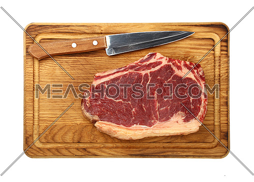 Close up one marbled raw ribeye beef steak with rib bone on wooden cutting board with knife, isolated on white background, elevated top view, directly above