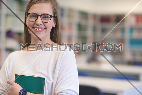 portrait of happy smilling female student girl in school library bholding book