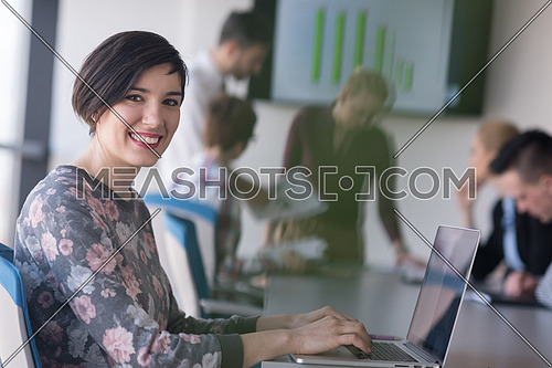 young  business woman at modern startup office interior working on laptop computer, blured team in meeting, people group in background