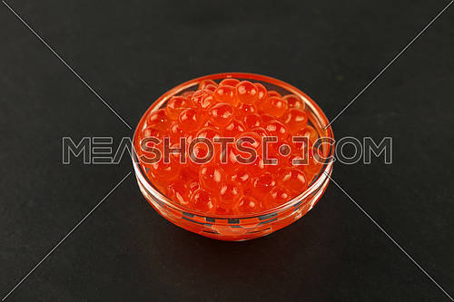 Close up one glass bowl of salmon fish red caviar on background of black slate kitchen board, high angle view
