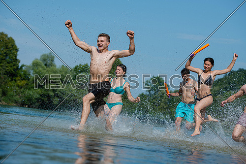 summer joy group of happy friends having  fun while running and splashing on river