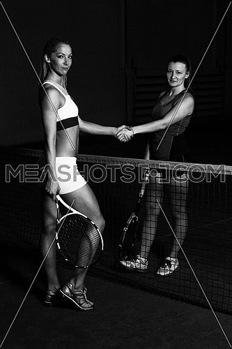 Two Beautiful Female Tennis Players Holding Rackets And Shaking Hands Over The Net - Isolated On Black