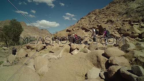 Long shot for group of tourists climbing down big rocks with bedouin guide to explore Sinai Mountain for wadi Freij at day.