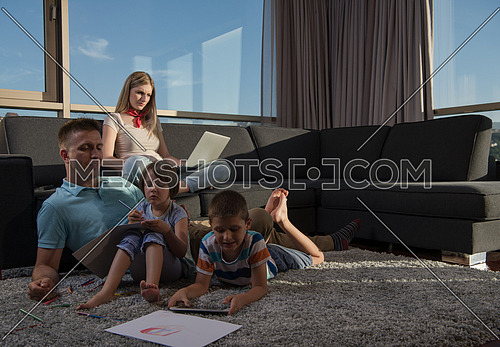 Happy Young Family Playing Together at home on the floor using a laptop computer and a children's drawing set