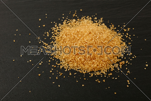 Close up pinch of brown cane sugar spilled on black slate board, high angle view