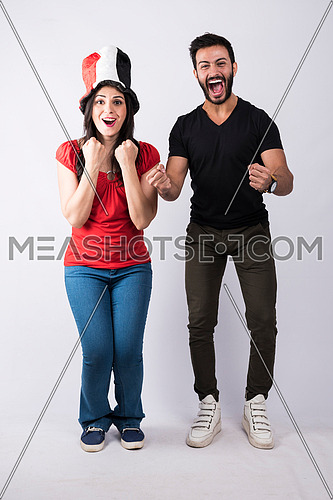 young couple standing and cheering, while the female wearing egyptian flag hat on white background