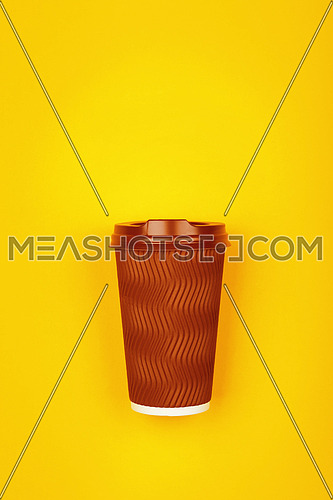 Close up one crimped disposable brown paper takeaway coffee cup over vivid yellow background, flat lay, elevated top view, directly above