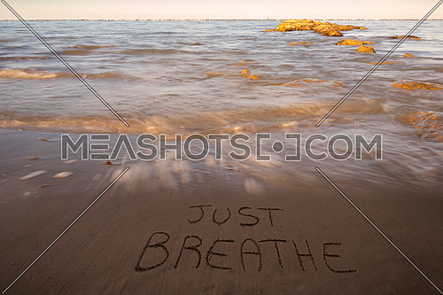 Handwritten Just breathe on sandy beach at sunset,relax and summer concept,Italian adriatic sea.