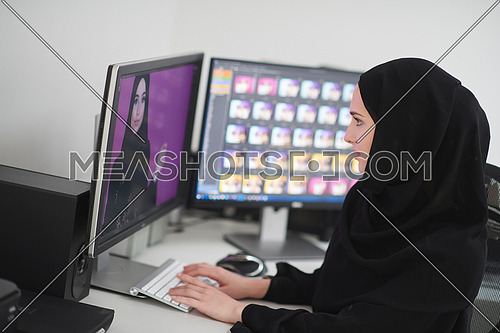 Young muslim girl working on the computer from home. Female photo editor at working place. Freelancer using two monitors while doing job