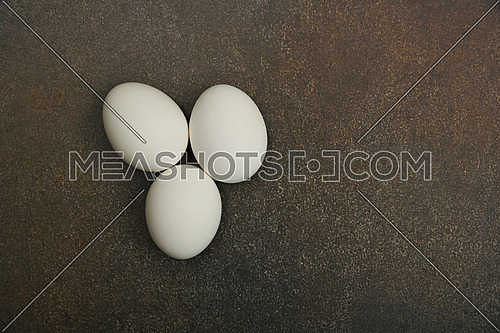 Close up three white chicken eggs on dark grunge table surface, elevated top view, directly above