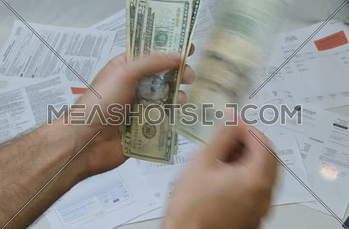 Close shot for a male hand holding Money (US Dollars) and throwing them on a table cover with a lot of Bills papers