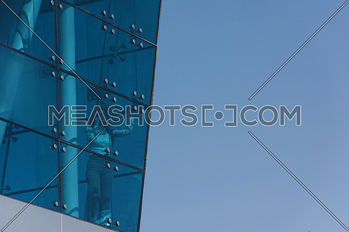 Outdoor shoot showing a female executive talking on the phone through the glass front of a corporate offices building with a background of blue sky
