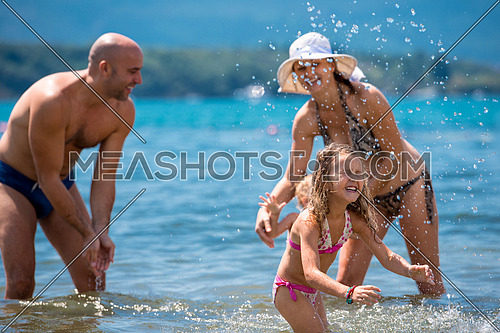 young happy couple with cute little daughters having fun while splashing each other in the shallow water of the sea during Summer vacation  Healthy family holiday concept