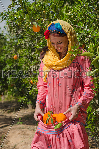a female egyptian farmer carying oranges in her traditional dress